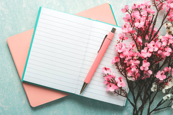 Draufsicht des leeren Journals geöffnet mit rosa Stift, Mandelblüten und Kopierraum über blauem Hintergrund - Foto, Bild