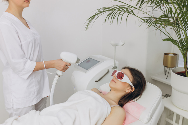 A woman tunes a laser hair removal machine. Girl holding a working part of the epilator in a modern beauty salon. Hair removal, laser procedure at medical clinic, spa concept. Laser skin care banner - Photo, Image