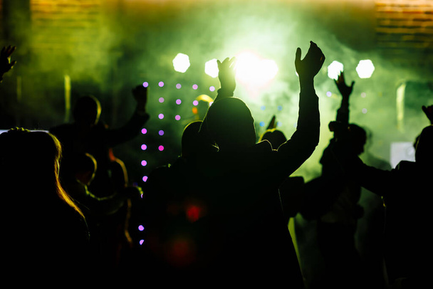 Jubelnde Menge vor leuchtend gelben Bühnenlichtern. Silhouette Bild von Menschen tanzen in Disco Nachtclub oder Konzert auf einem Musikfestival - Foto, Bild