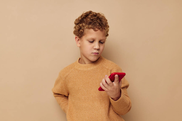 мальчик в свитере с телефоном в руках технологии бежевого фона - Фото, изображение