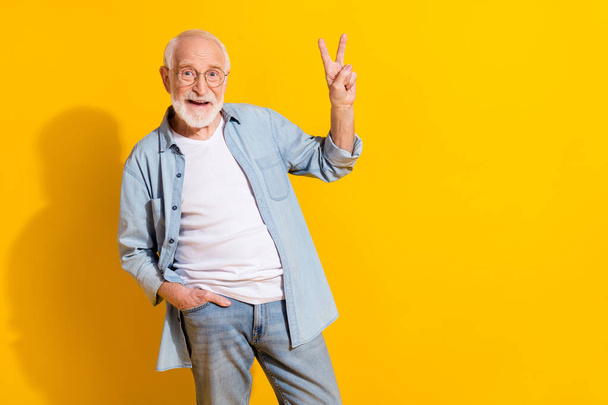 Portrait of attractive funky cheerful grey-haired man showing v-sign good mood isolated over bright yellow color background - Zdjęcie, obraz