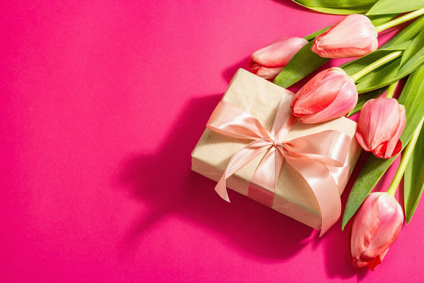 Gruß Konzept Blumenkomposition, ein Strauß rosa Tulpen und ein Geschenk. Weltfrauentag, Valentinstag oder Muttertag, Hochzeit. Magenta Hintergrund, flache Lage - Foto, Bild