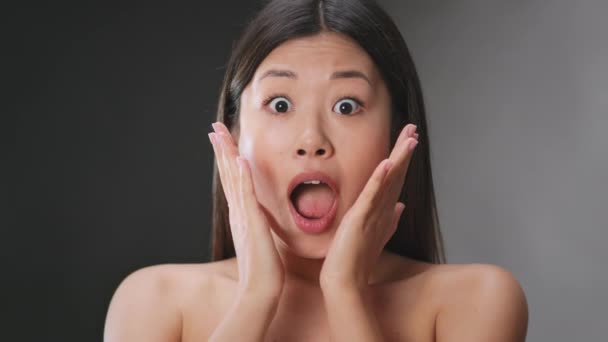 Портрет молодої здивованої азіатки відчуває шок і невіру, відкриваючи рот і торкаючись її щоки в невірі
 - Кадри, відео