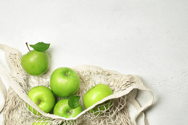 軽いコンクリートのテーブルの上のメッシュバッグの中の新鮮な緑のリンゴ - 写真・画像