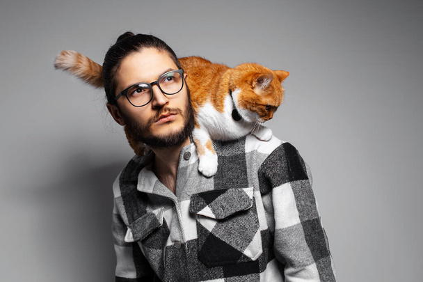 Portrait of young attractive man with his red cat on the shoulders. - Photo, Image