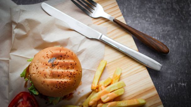 Házi készítésű hamburger sült krumplival és paradicsommal egy fa asztalon. Gyorsétterem és gyorsétterem. - Fotó, kép