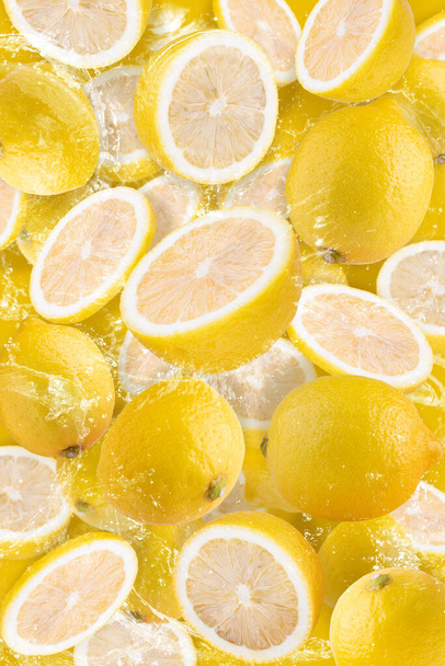 Salpicaduras de agua sobre fruta de limón en rodajas aisladas sobre fondo amarillo - Foto, Imagen