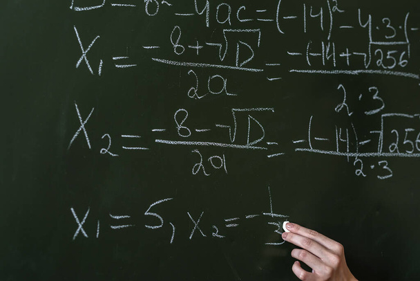 schoolgirl writing high school maths formula  with chalk on blackboard, Math class algebra - Valokuva, kuva
