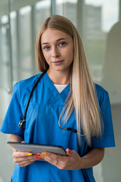 bella giovane infermiera con uno stetoscopio e una tavoletta si trova nel corridoio. Concetto di medicina - Foto, immagini