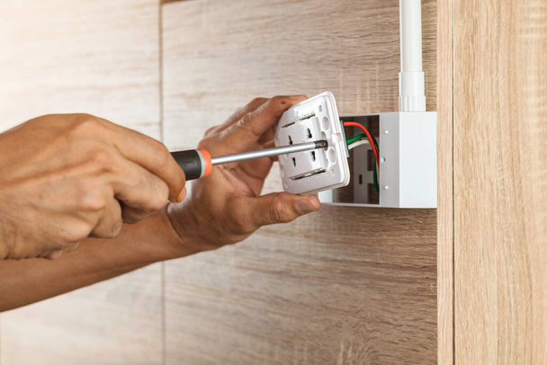 Elektricien gebruikt een schroevendraaier om een stopcontact in een plastic doos op een houten muur te monteren. - Foto, afbeelding