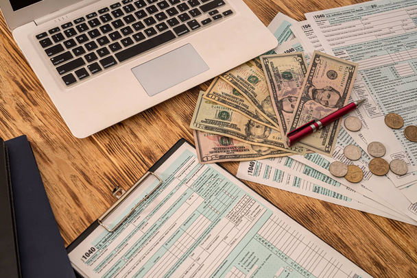 Weißes Notizbuch Steuerformular USA 1040 mit Dollarscheinen und Münzen auf einem Holztisch ausgebreitet. Geschäftskonzept - Foto, Bild