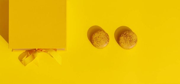 Caja de regalo amarilla con lazo de cinta y dos macarrones franceses sobre fondo amarillo. Saludo para el Día Internacional de la Mujer el 8 de marzo, día de la madre, cumpleaños, Pascua o concepto de primavera. Copiar espacio - Foto, Imagen