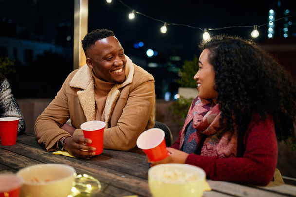 Biracial female and black male talking while at a rooftop party in the city. Trendy, drinking with red cups. - Fotó, kép