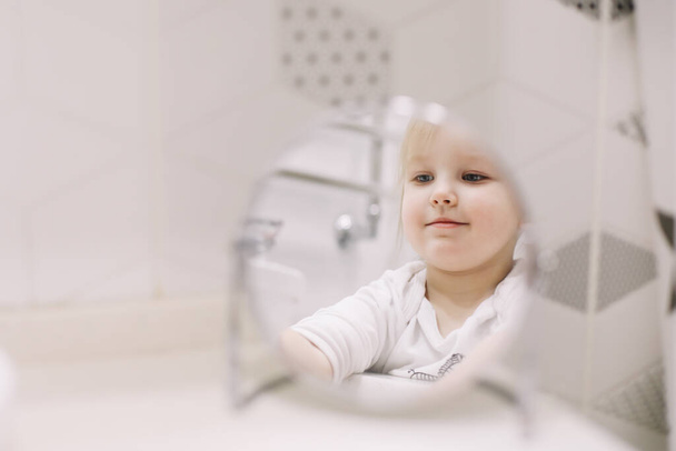 little funny girl brushing teeth and washing hands in the bathroom, reflection in the mirror - Foto, imagen