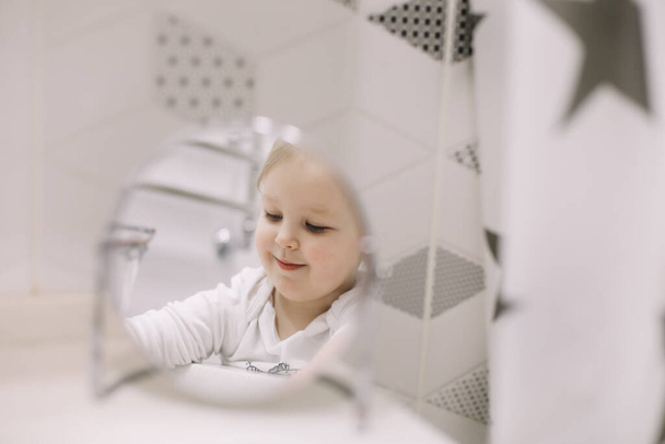 little funny girl brushing teeth and washing hands in the bathroom, reflection in the mirror - Fotografie, Obrázek