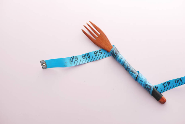 fork with measurement tape on pink background  - Фото, изображение