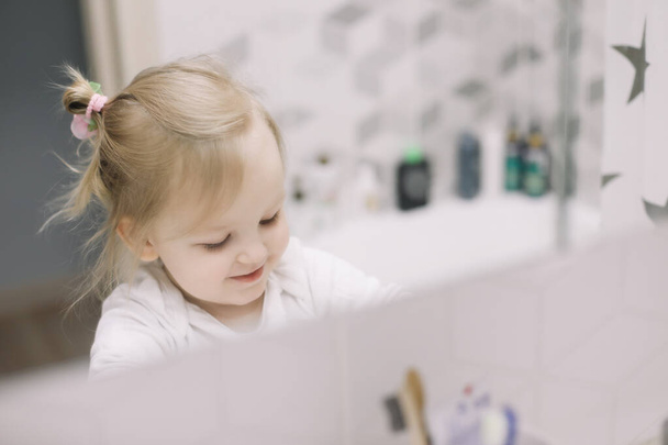 little funny girl brushing teeth and washing hands in the bathroom, reflection in the mirror - Fotografie, Obrázek