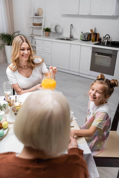 Neşeli bir kadın elinde bir sürahi portakal suyu, neşeli bir kız ve bulanık bir anne tutuyor. - Fotoğraf, Görsel