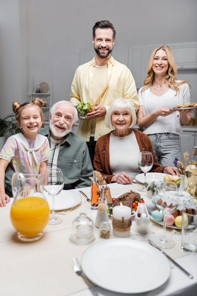 happy family smiling at camera near table served with easter dinner - Фото, зображення