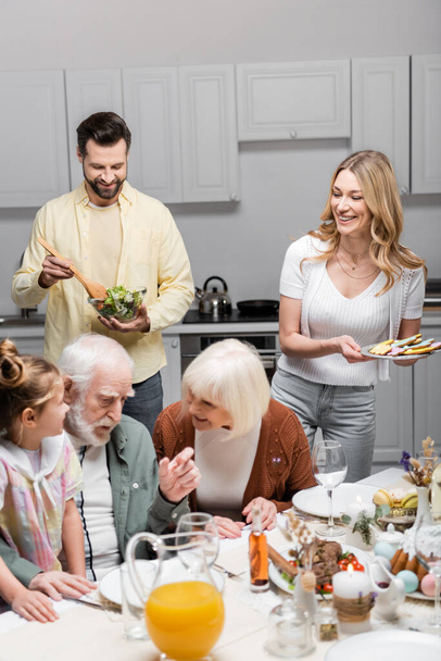 smiling man mixing vegetable salad during family easter dinner  - Photo, Image