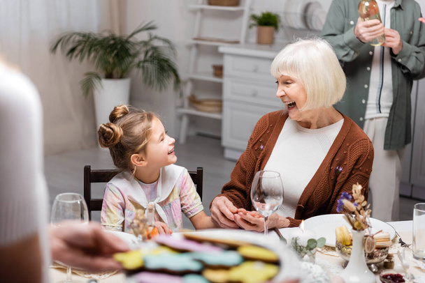 excited woman talking to granddaughter during easter celebration with family - Фото, изображение