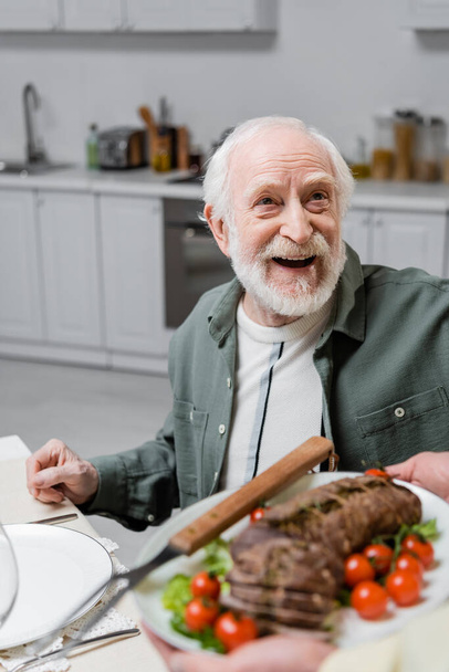 elképedt idősebb férfi nézi feleség gazdaság lemez hússal húsvéti ünnepség - Fotó, kép
