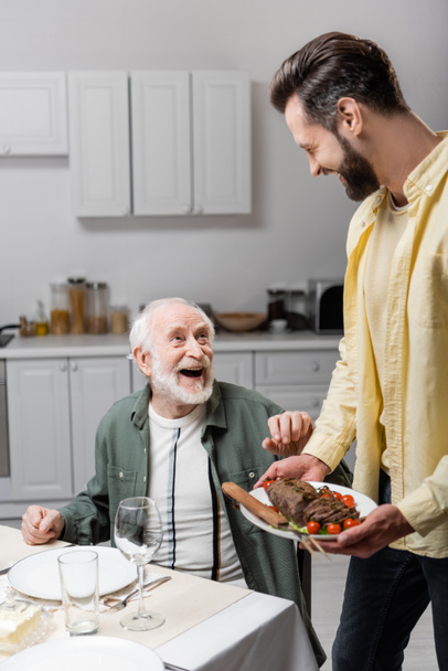 man holding plate with fried meat during easter dinner with laughing father - Φωτογραφία, εικόνα