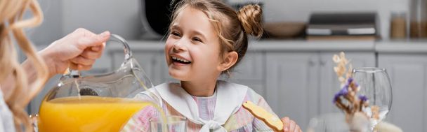 girl smiling near mother pouring orange juice during easter dinner, banner - Foto, immagini