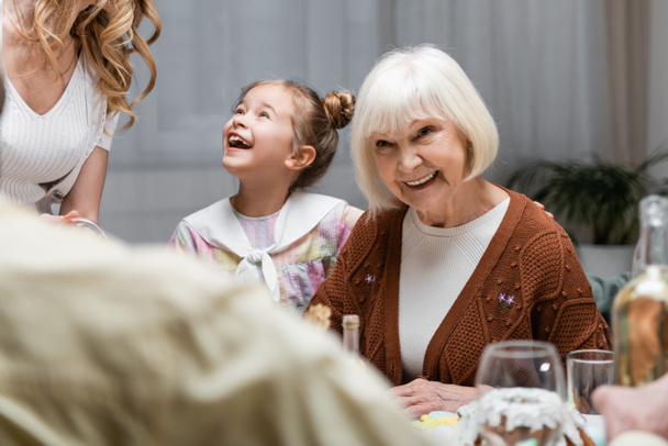 starší žena usmívá téměř ohromený vnučka při slavnostní večeři s rodinou - Fotografie, Obrázek