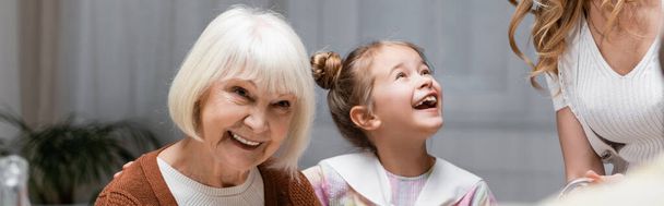 chica emocionada cerca de la abuela sonriente y la madre en casa, pancarta - Foto, imagen