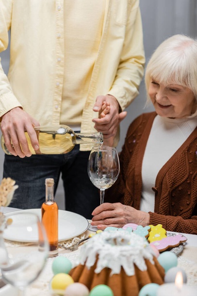 man pouring wine while holding hand of senior mother during easter dinner - 写真・画像