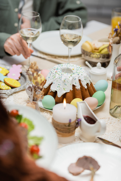 partial view of man near delicious easter cake, painted eggs and wine glasses on festive table - Photo, image