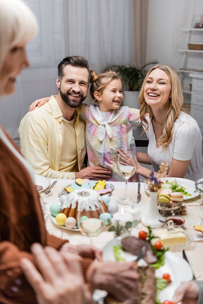 girl smiling near happy parents during easter dinner on blurred foreground - Fotoğraf, Görsel