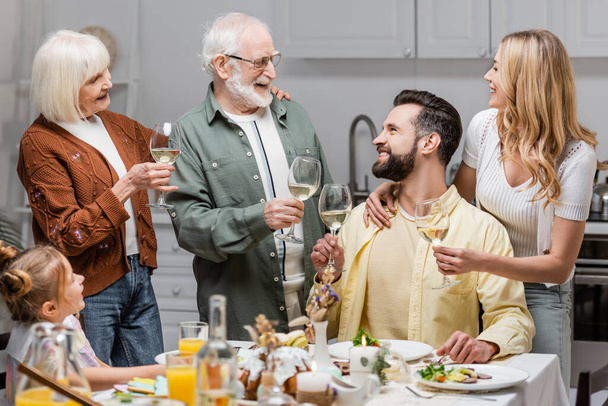 excited family holding wine glasses while toasting during easter dinner - Foto, imagen