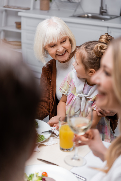 cheerful senior woman hugging granddaughter while celebrating easter with family - Фото, изображение