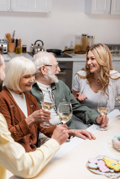 イースターディナーの間にワインとグラスを持っている先輩の両親と話す幸せな女性 - 写真・画像