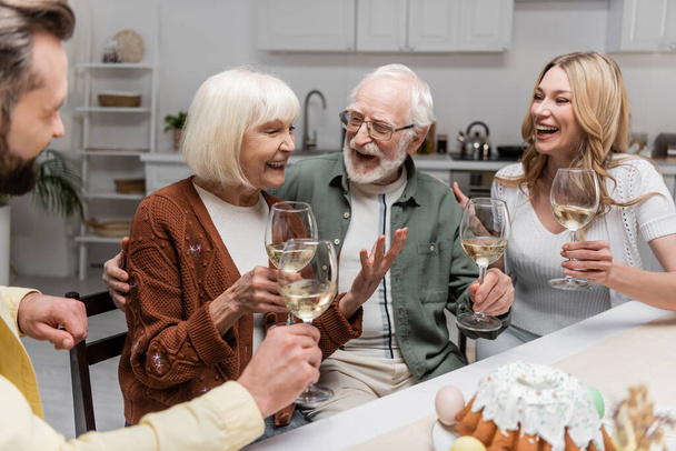senior woman holding glass of wine and laughing during family dinner - Foto, afbeelding