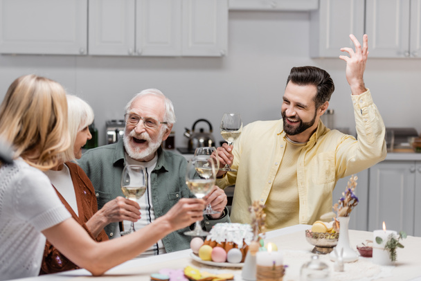 excited man gesturing with raised hand near family toasting with wine glasses - Foto, Bild