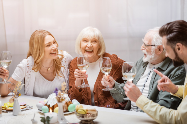 homem apontando com o dedo perto de família feliz segurando copos de vinho durante o jantar festivo - Foto, Imagem