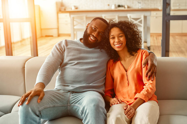 African American couple sitting on sofa and hugging in living room at home. - Zdjęcie, obraz