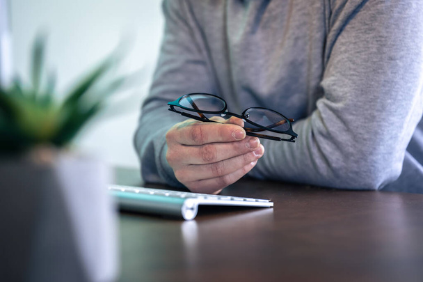 Szemüveg férfi kezekben a munkahelyen, a számítógép előtt. - Fotó, kép