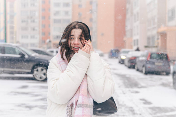 Портрет девочки-подростка на улице со смартфоном в снежную зимнюю погоду. - Фото, изображение
