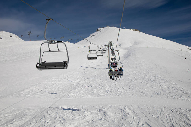 Wyciąg narciarski pusty ropeway na wzgórzu alpejski ośrodek zimowy w jasny słoneczny wieczór. Wyciąg krzesełkowy sposób z ludźmi cieszyć się narty i snowboarding. - Zdjęcie, obraz