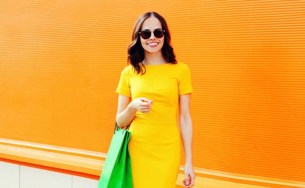 Portrait of beautiful young woman with shopping bags on colorful orange background - Foto, Imagem