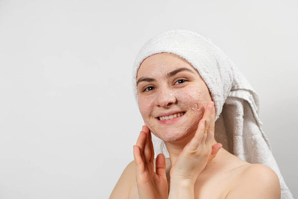 Μια όμορφη νεαρή γυναίκα εφάρμοσε ένα scrub ή μάσκα στο πρόσωπό της, περιποίηση προσώπου, καθαρισμό του δέρματος - Φωτογραφία, εικόνα
