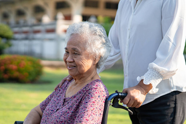 Aide et soins aux aidants aînés asiatiques ou vieille dame patiente assise sur un fauteuil roulant dans un parc, concept médical solide et sain. - Photo, image