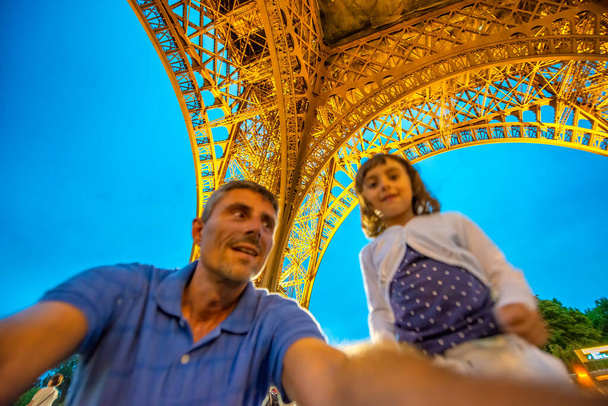Mężczyzna z córką pod Wieżą Eiffla w nocy - Zdjęcie, obraz