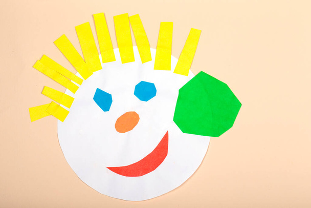 Paper crafts for children. Application of children's creativity. Kindergarten and craft school. On a beige background, a funny face of a man made of colored paper. - 写真・画像