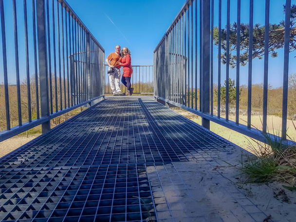 Metal vyhlídka v dunách zépheduinen Burgh-Haamstede, s úsměvem multikulturní pár při pohledu na kameru z nižší perspektivy, slunečný den s modrou oblohou na Zélandu, Nizozemsko - Fotografie, Obrázek