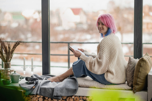 Una ragazza con un maglione bianco seduta vicino alla finestra - Foto, immagini